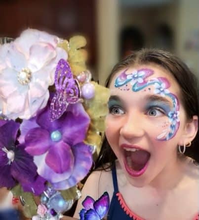 Butterfly and Floral Face Paint Design Young girl with purple and blue face paint smiling wide