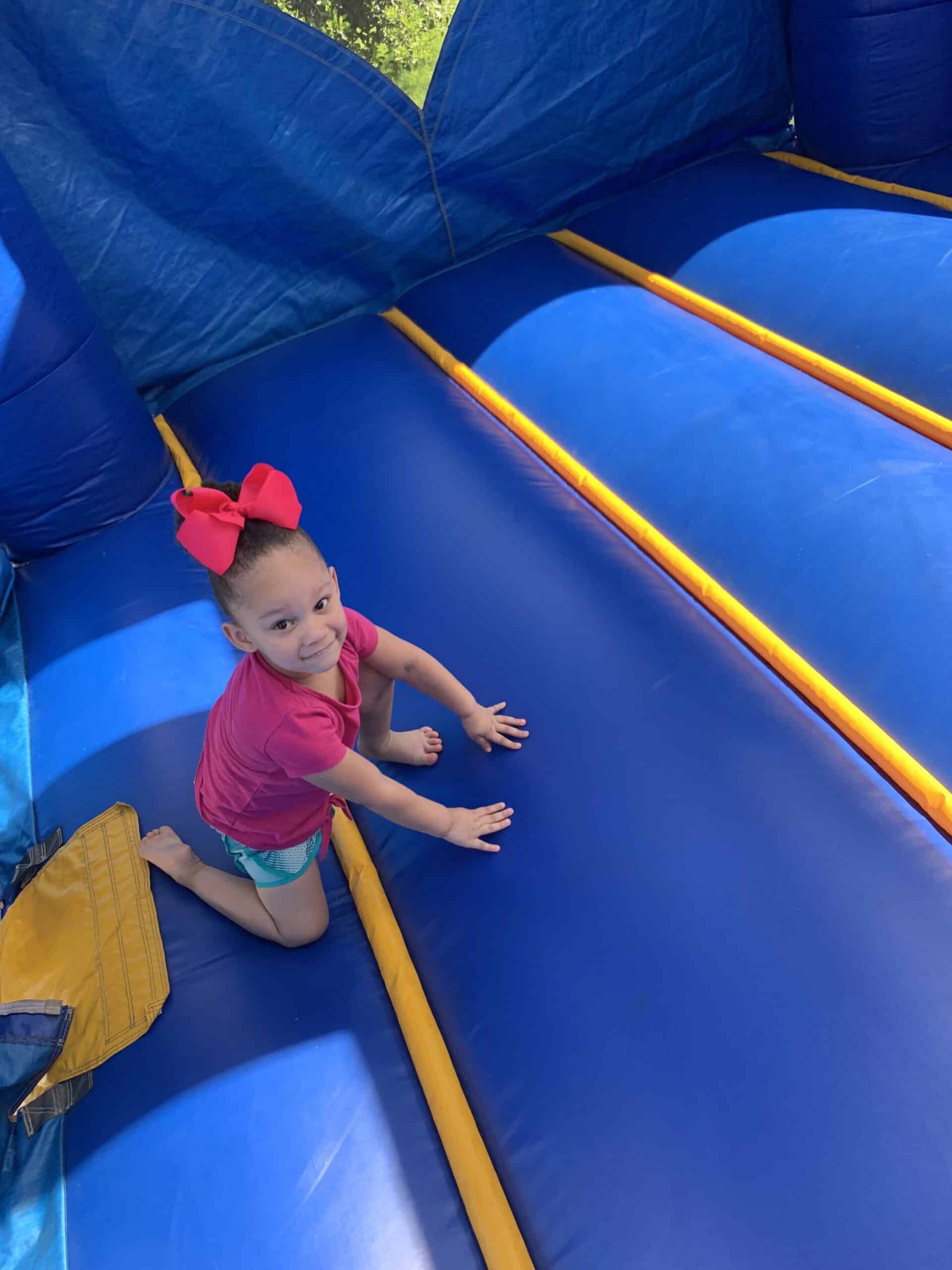 Young girl in a pink shirt smiling while playing inside a blue bounce house.