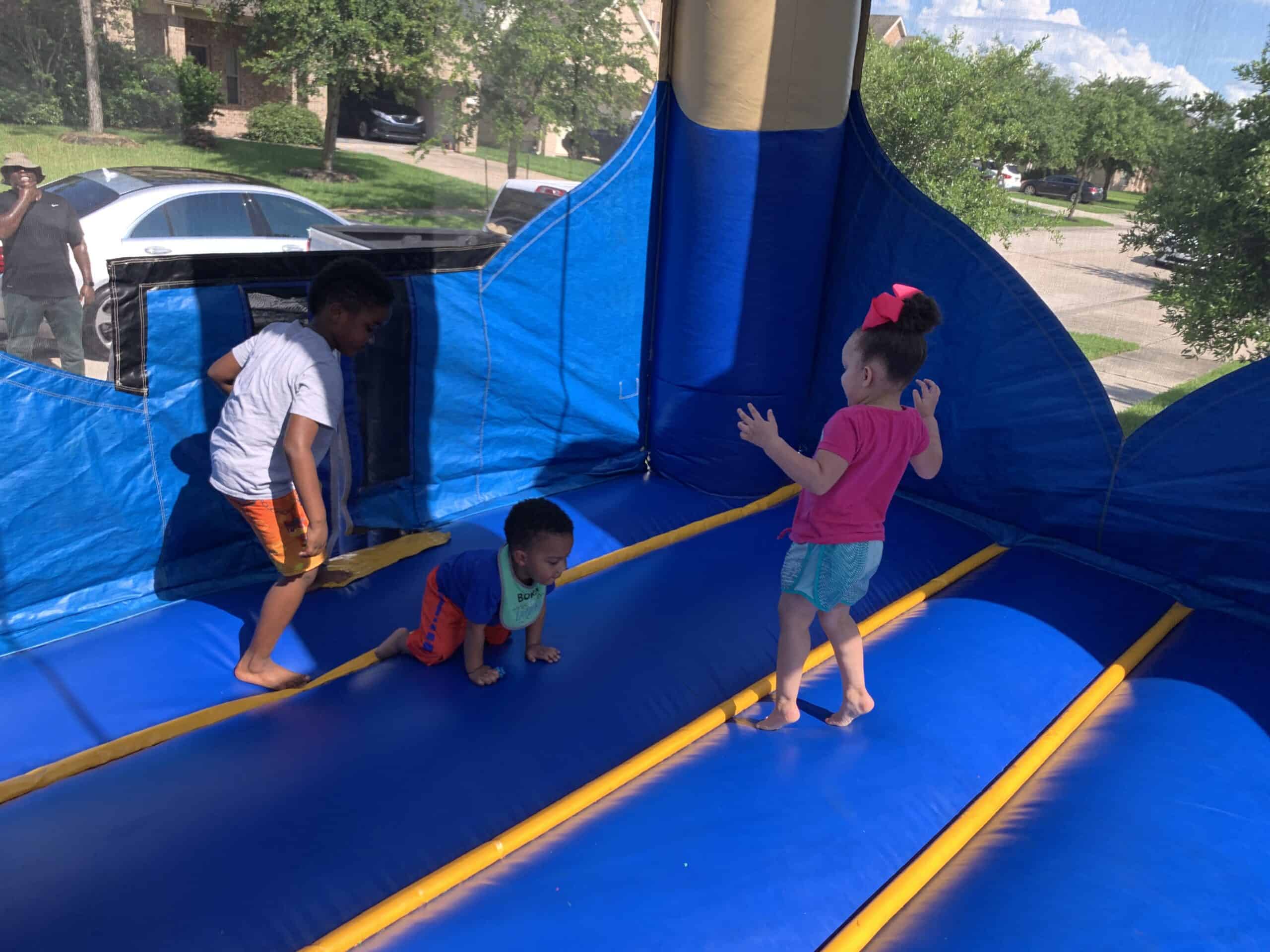 Three young children playing and jumping inside a blue inflatable bounce house