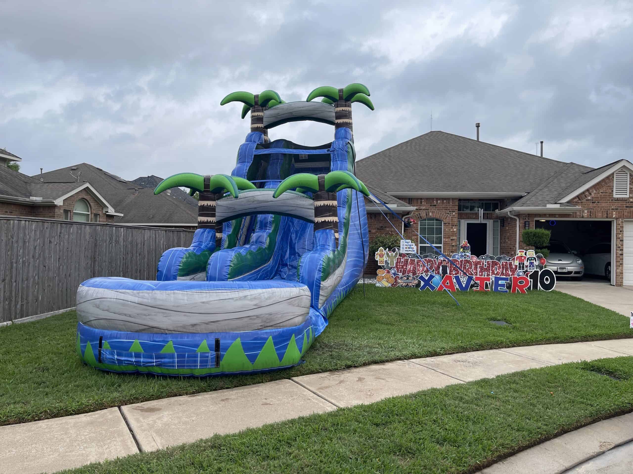 Tropical Water Slide with Birthday Signage Tropical water slide inflatable with a birthday lawn greeting display in front of a house