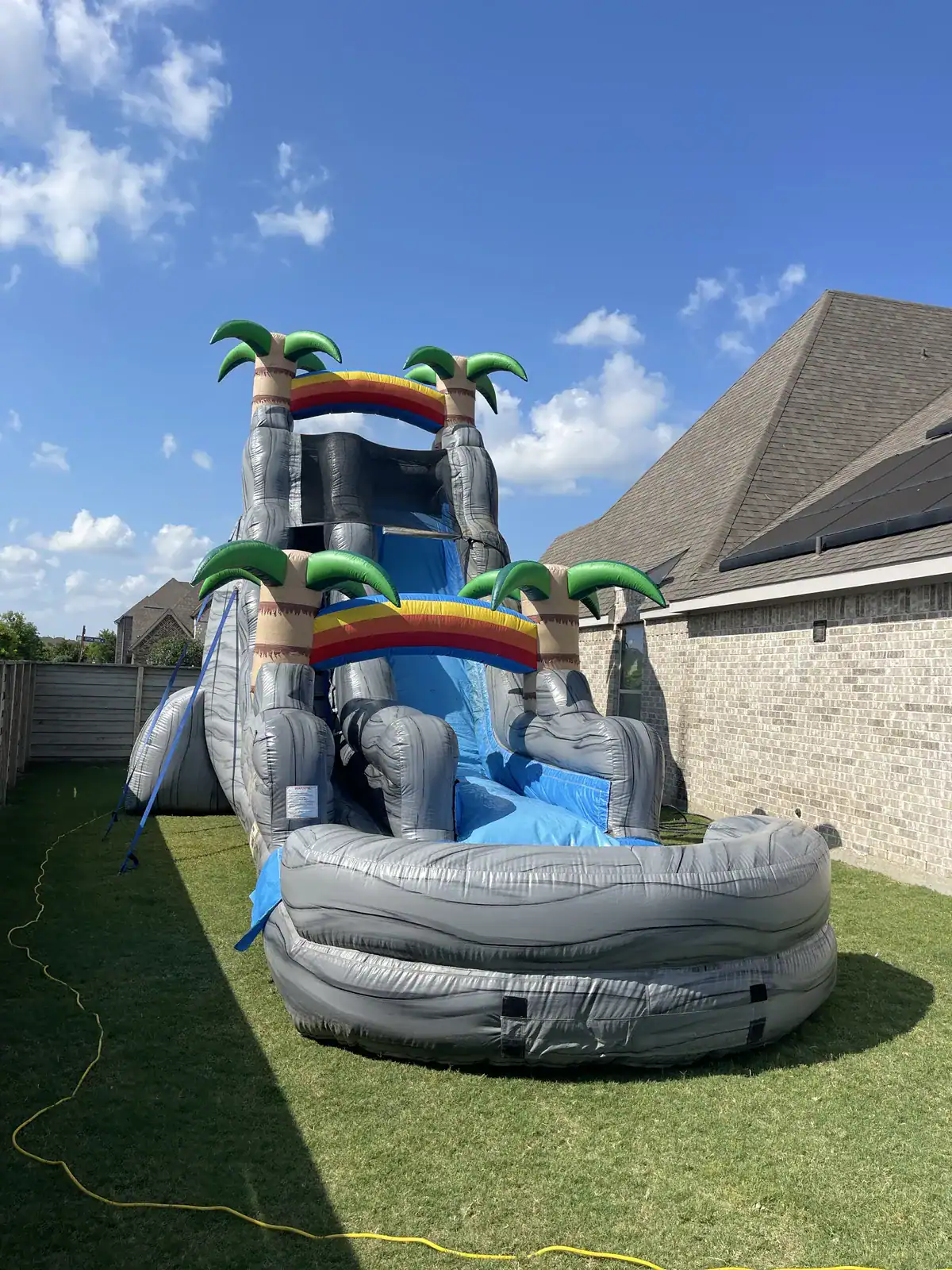 Party Kids America Water Slide Colorful inflatable water slide with palm trees and rainbows in backyard.