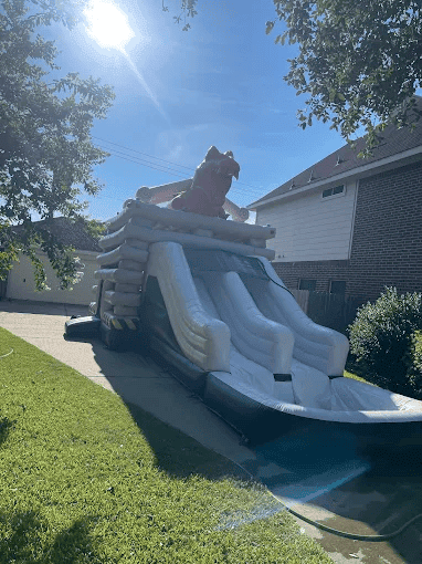 Inflatable T-Rex themed water slide in a backyard setting.